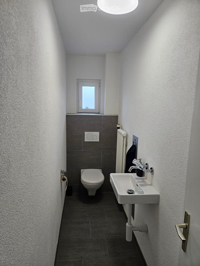 Modern bathroom with a toilet, sink, and radiator. Features a window above the toilet and a sleek, contemporary design.