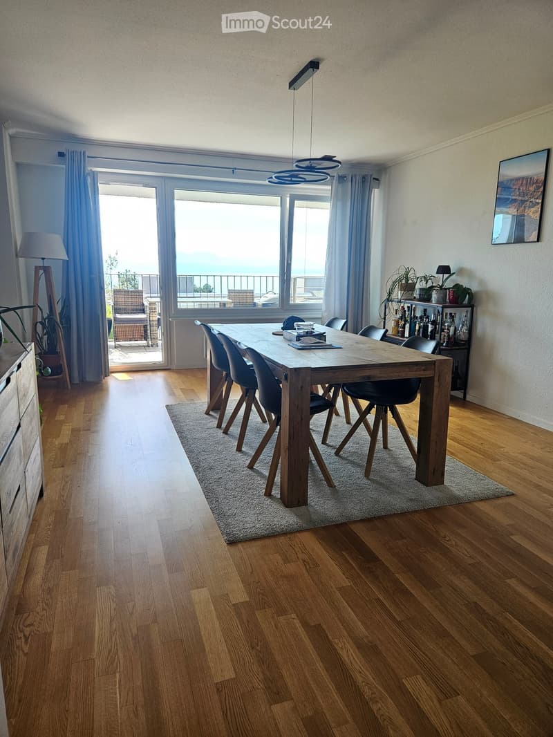 Dining room with wooden floor, large window with balcony access, dining table with chairs, cabinet, and decorative items.