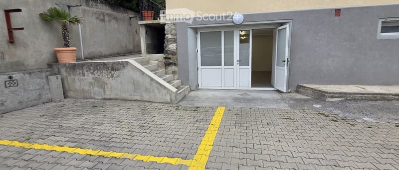 Exterior view of a building with a raised entrance, concrete steps, and a paved area with a marked parking space.