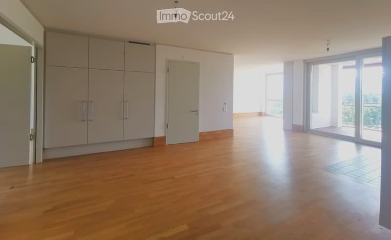 Empty room with wooden flooring, large windows, and a sliding glass door leading to a balcony.