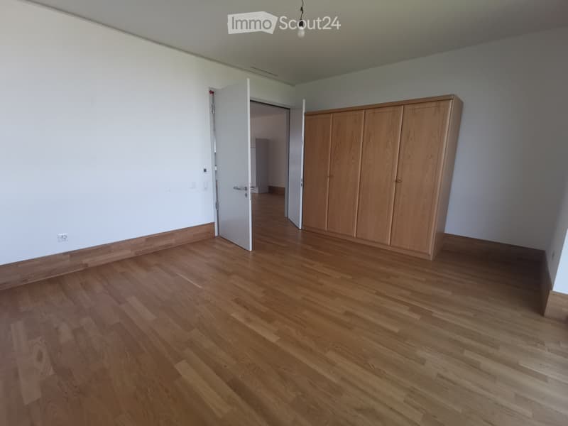 Empty room with wooden flooring, white walls, and a built-in wooden cabinet. The room has a door leading to another space.