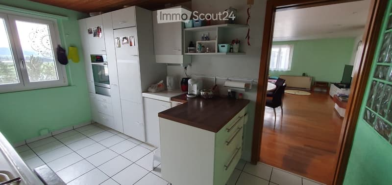 Bright kitchen with white cabinets, a dark wooden countertop, and a view of a living area with wooden flooring and a dining table.