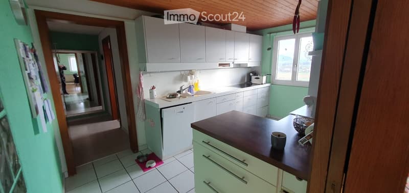 Bright kitchen with white cabinets, a dishwasher, sink, countertop, and various small appliances. The space features a wooden ceiling and a view into an adjacent room.