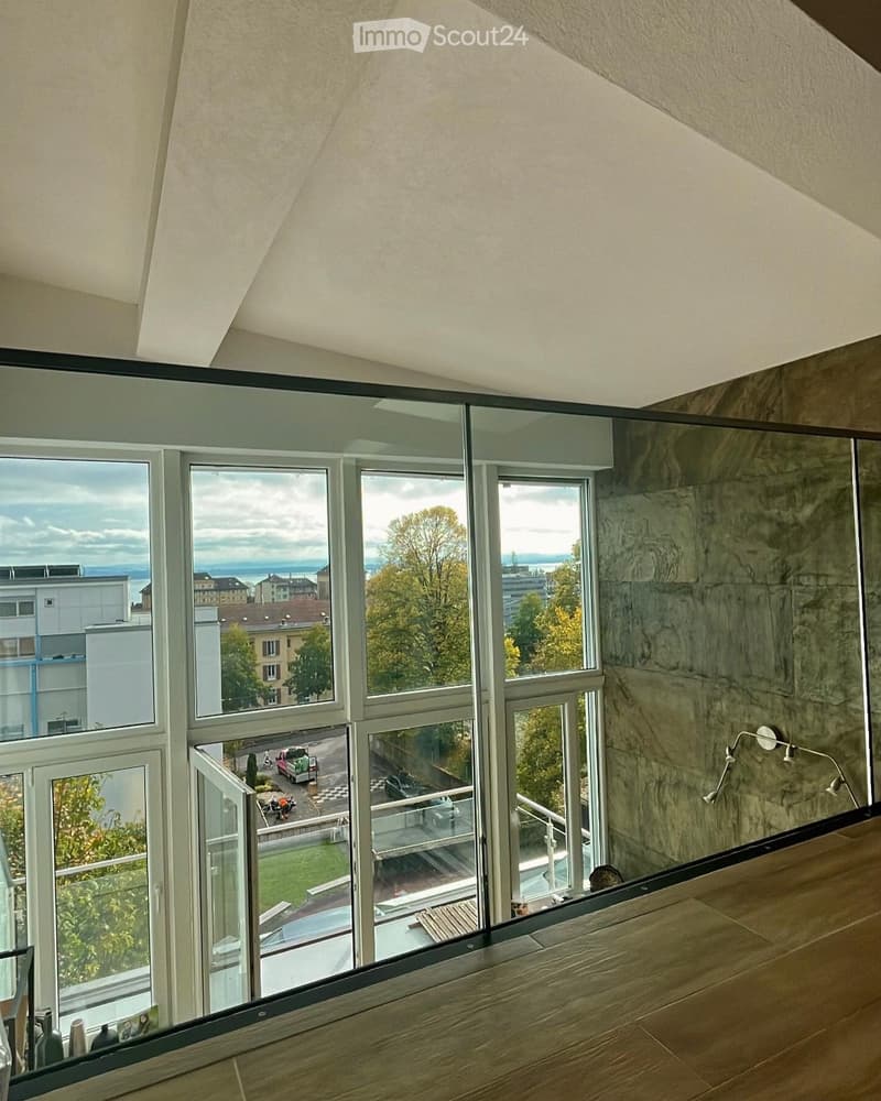 Modern hallway with large windows offering a view of the city and surrounding greenery. The walls are textured, and the floor is made of light wood.