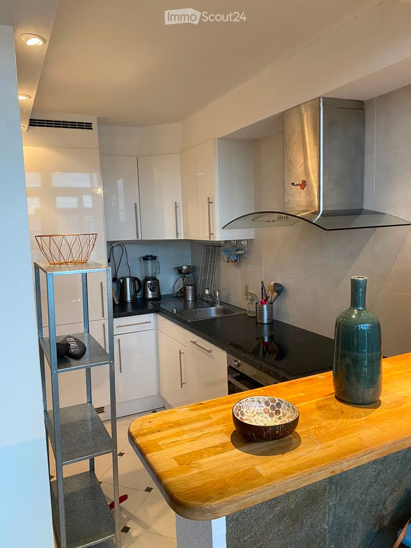 Modern kitchen with white cabinets, stainless steel appliances, wooden countertop, and various kitchen items including a blender, sink, stove, and decorative vase.