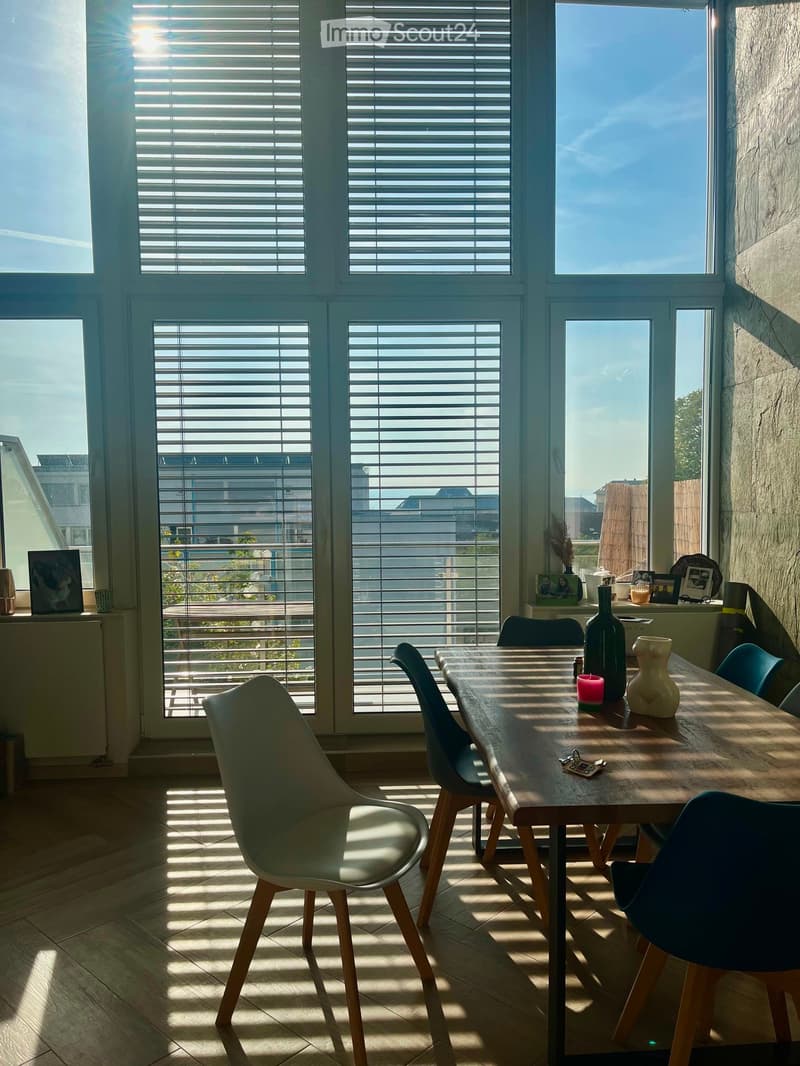 Bright dining area with large windows, wooden table, modern chairs, decorative items, and a view of the city.