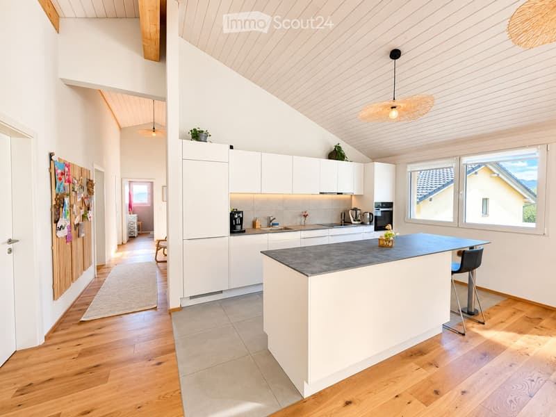 Modern kitchen with white cabinets, a central island, and wooden flooring. Features include a coffee maker, sink, oven, and a hanging wicker pendant light.