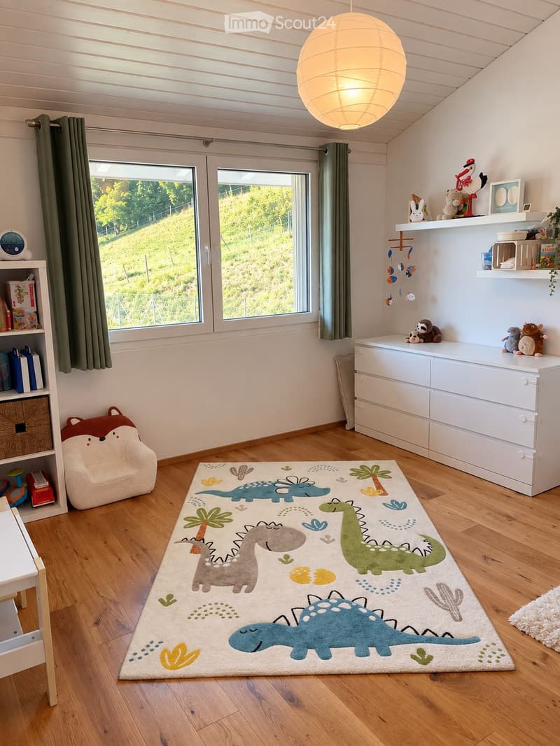 Brightly lit children's bedroom with wooden flooring, large windows, a dinosaur-themed rug, a plush chair, shelves with toys and books, and a hanging mobile.
