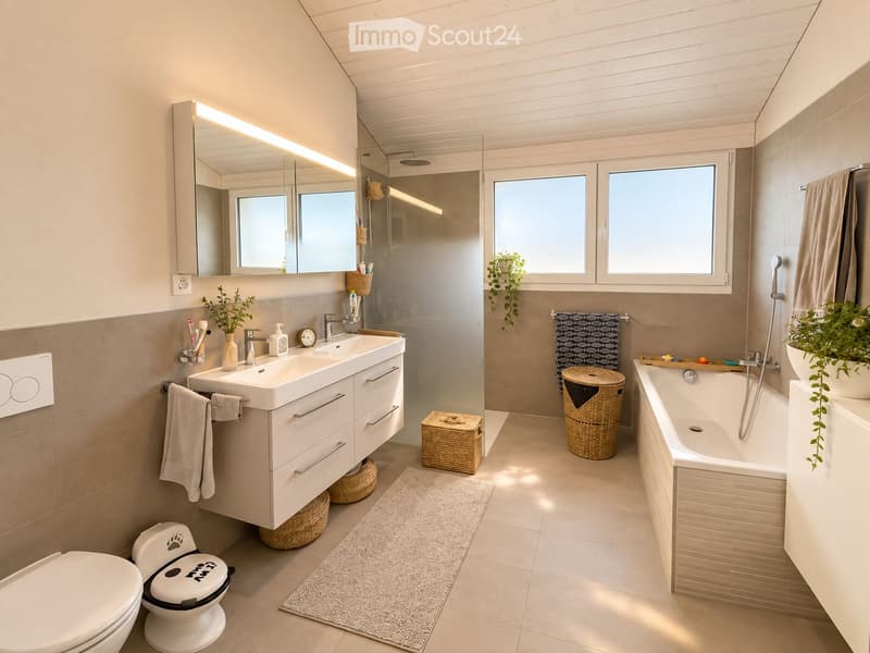 Modern bathroom with a double sink, large mirror, bathtub, toilet, and shower area. Features include wicker baskets, towels, and plants, with natural light from windows.