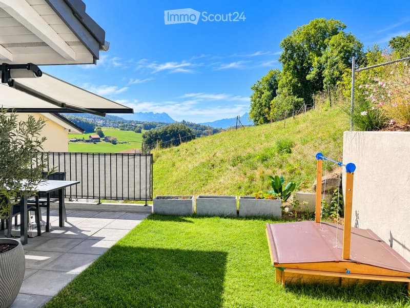 Garden with a patio area, outdoor furniture, and a scenic view of green fields and mountains.