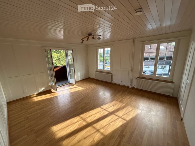 Empty room with wooden flooring, white walls, large windows, and an open door leading outside.