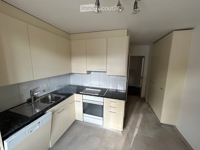 Modern kitchen with white cabinets, black granite countertops, stainless steel sink, oven, and dishwasher. The space is well-lit with recessed lighting.