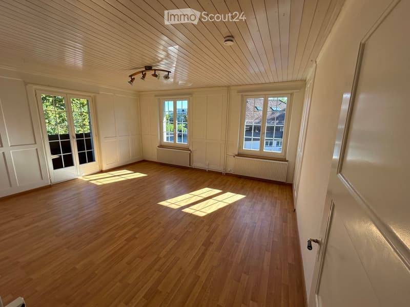 Empty room with wooden flooring, white walls, large windows, and a radiator. No furniture or equipment present.
