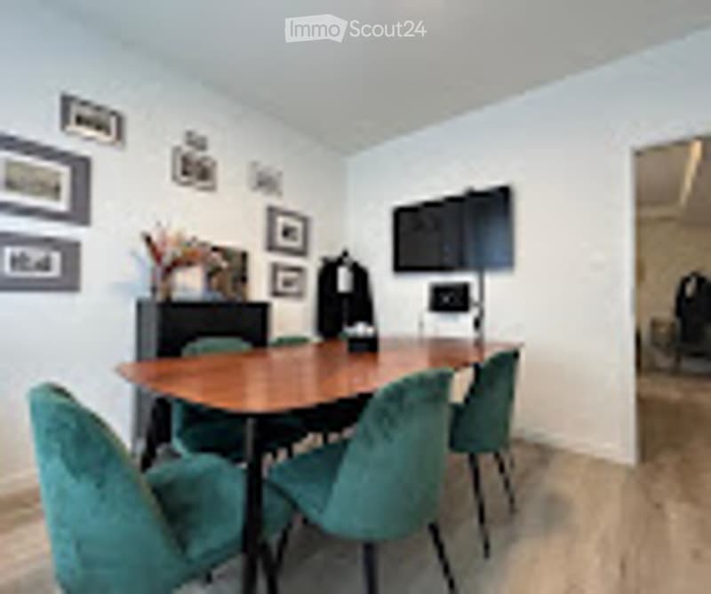 Dining room with a wooden dining table, four matching chairs, a mounted television, and several picture frames on the wall.