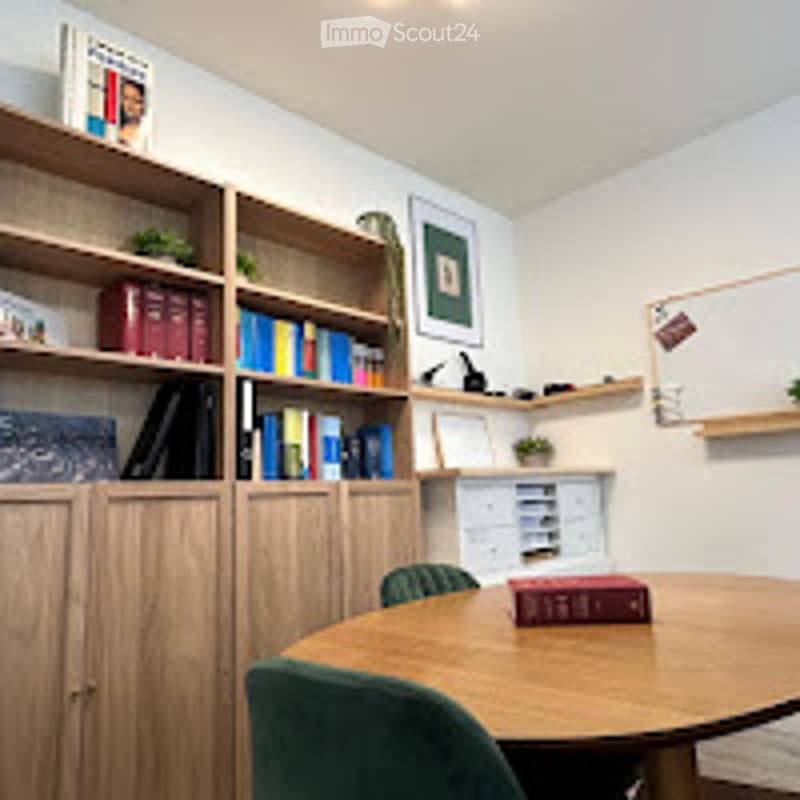 A cozy study or home office with wooden built-in bookshelves, a round wooden table, and green chairs.
