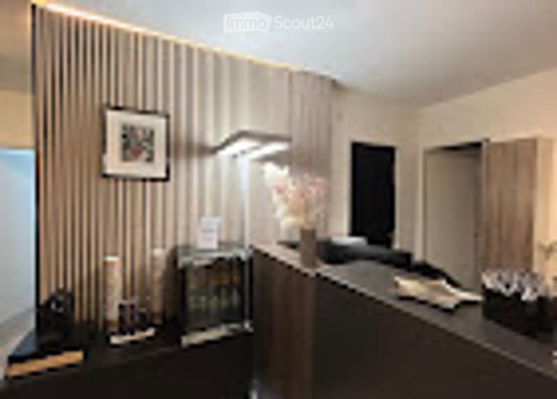 Modern living room with a grey sofa, coffee table, wall-mounted TV, side table, and floor lamp. The room features large windows and a decorative picture on the wall.