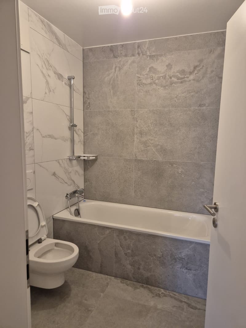 Modern bathroom with marble tiles, a bathtub, toilet, and a shower handle.