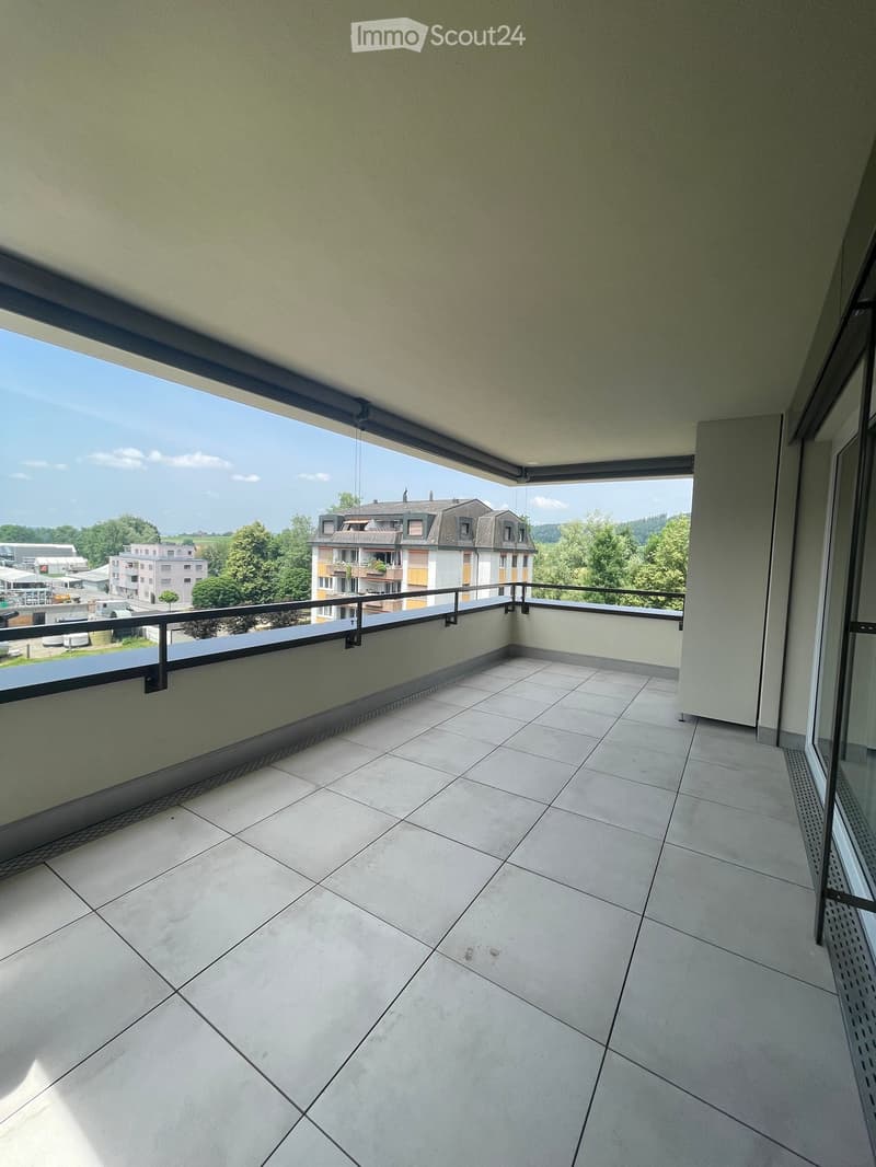 Empty balcony with tiled floor, metal railing, and a view of the surrounding area and buildings.