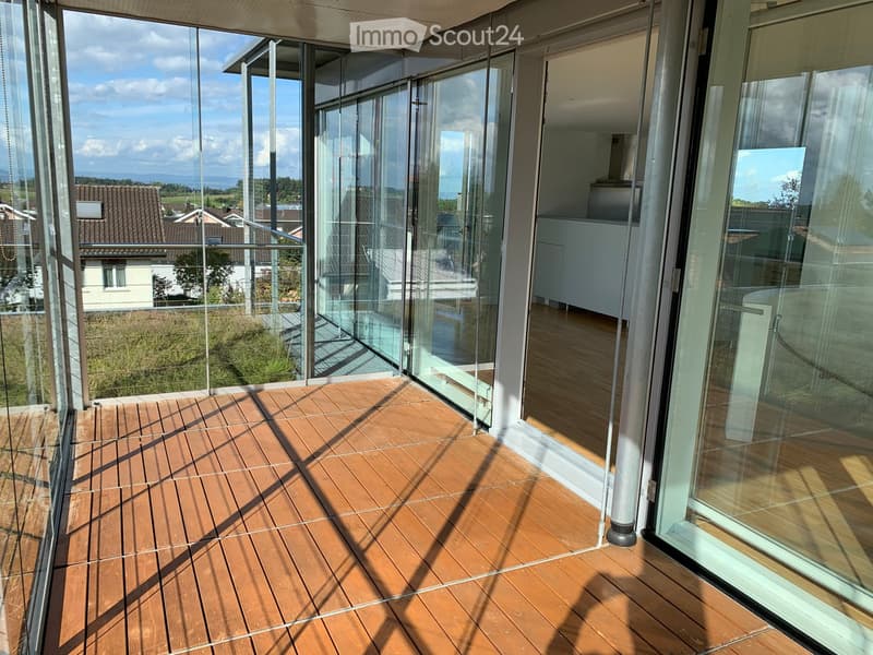 Modern balcony with wooden decking, large glass sliding doors, and a view of the surrounding landscape.