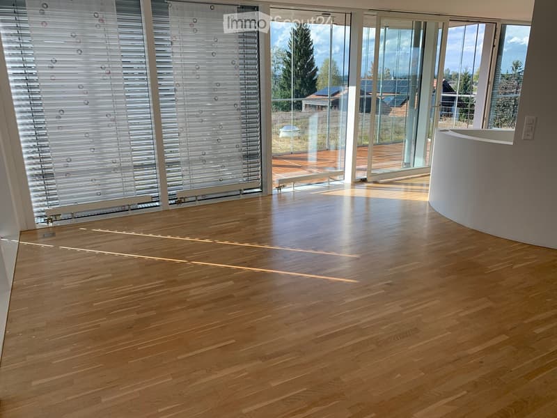 Empty room with light wooden flooring, large glass sliding doors leading to a wooden deck, and a white curved wall on the right side.