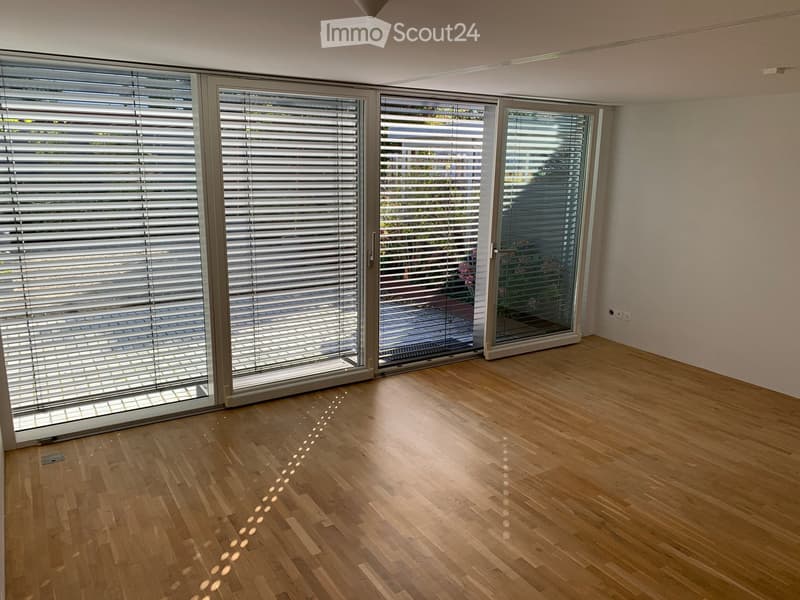 Empty room with wooden flooring, large sliding glass doors with blinds, and white walls.