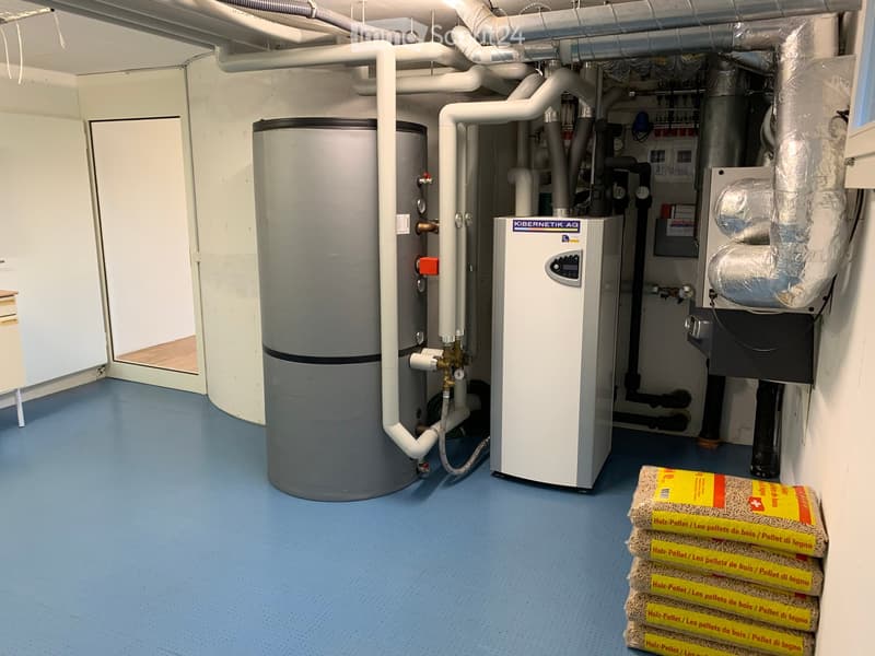 Utility room with a water heater, control unit, and stacked bags of wood pellets on the floor.