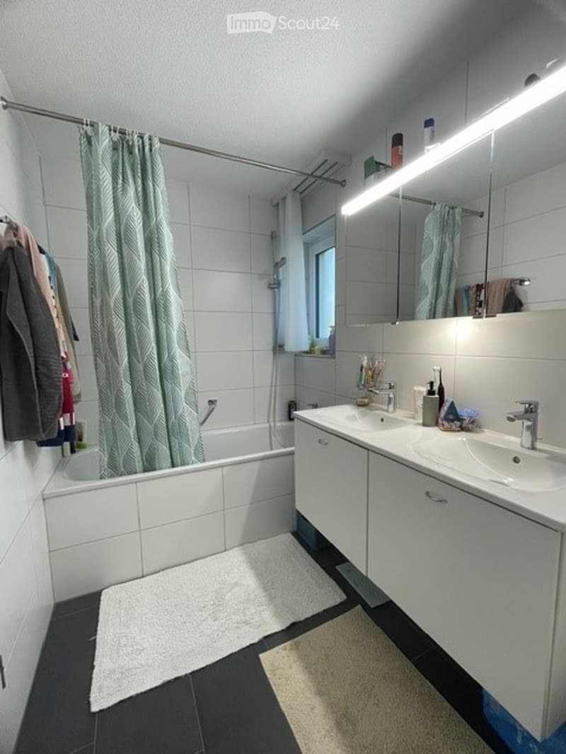 Modern bathroom with white tiles, a bathtub, double sink, mirrored cabinet, and a window with a green curtain.