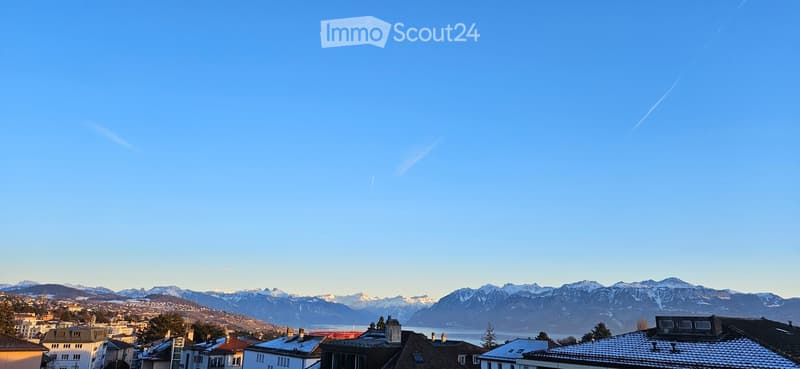 Panoramic view of a town with snow-capped mountains and a lake in the background under a clear blue sky.