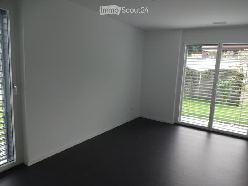 Empty room with white walls, dark flooring, and large sliding glass doors leading to an outdoor area.