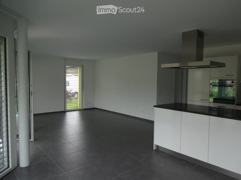 Modern kitchen with white cabinets, black countertop, dark tiled floor, and a central island. Features a built-in range hood and large windows with blinds.