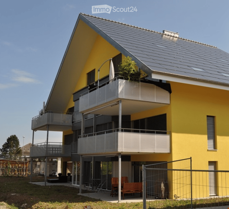 Modern two-story house with yellow and grey exterior, multiple balconies, and outdoor seating area.