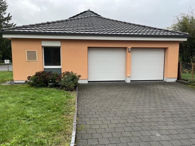 Single-story house with a tiled roof, peach-colored exterior, white garage doors, and a paved driveway.