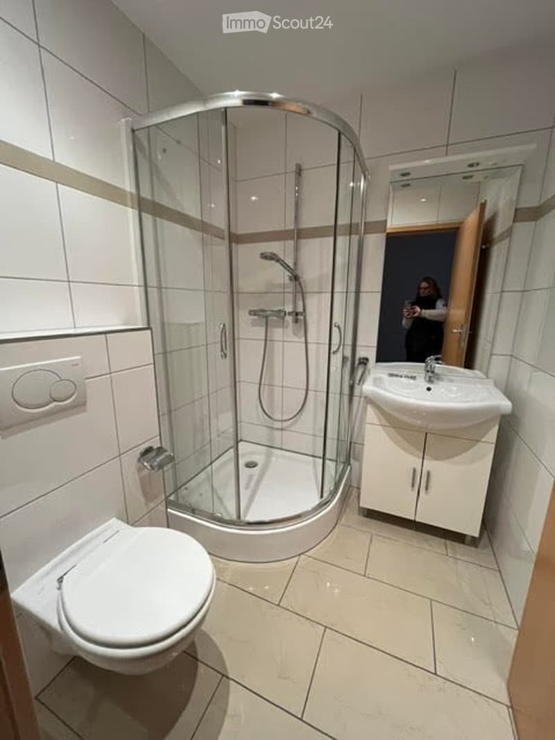 Modern bathroom with white tiles, a corner shower, toilet, sink, and mirrored cabinet.