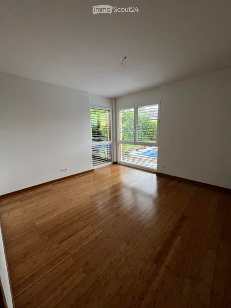Empty room with wooden flooring, white walls, large windows, and sliding doors leading to a balcony and pool area.