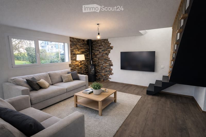 Modern living room with a grey sofa, coffee table, armchair, TV, floor lamp, and a fireplace with a view of the garden.