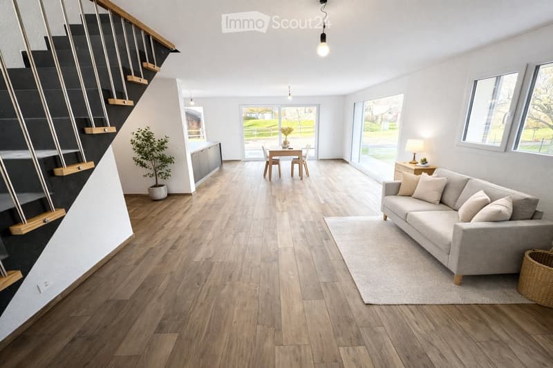 Modern living room with wooden flooring, grey sofa, coffee table, dining area, and large windows overlooking a green landscape.