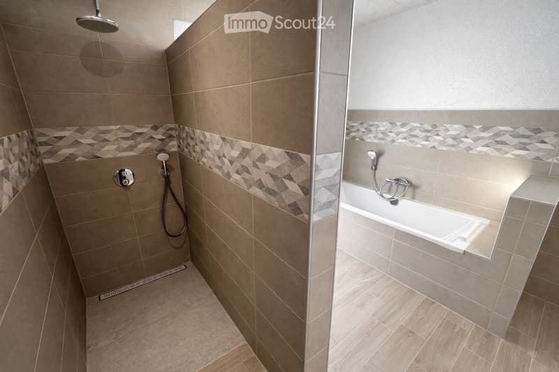 Modern bathroom with a bathtub and separate shower area, featuring beige tiles and geometric patterned borders.