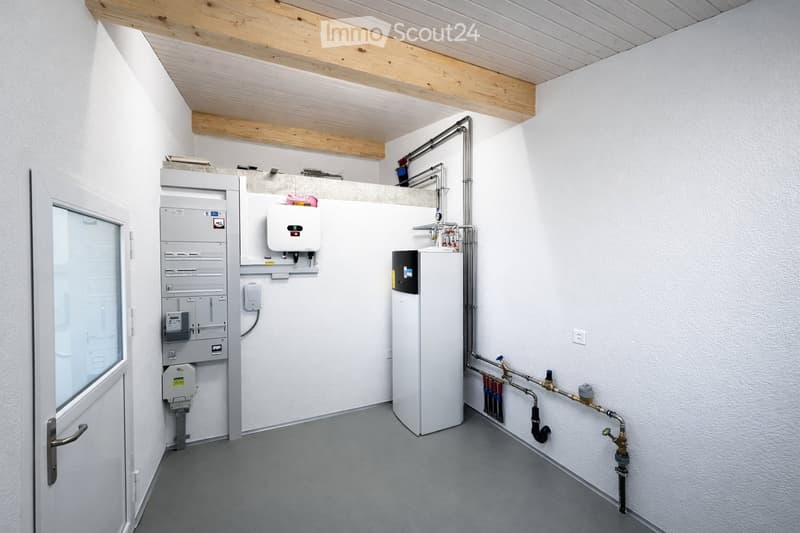 Utility room with white walls, grey floor, wooden ceiling, electrical panel, water heater, and various pipes.