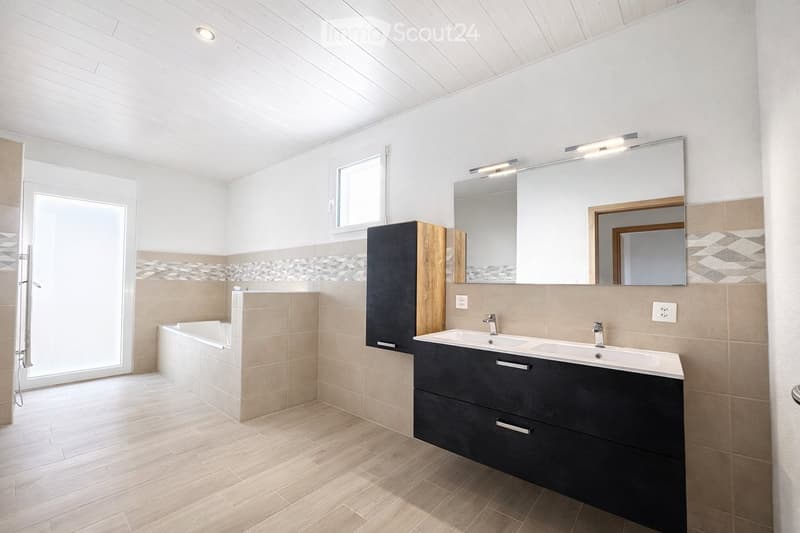 Modern bathroom with a bathtub, double sink, large mirror, and dark wooden cabinet.