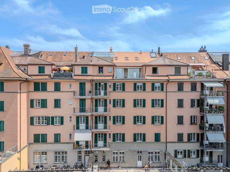 Multi-story residential building with pink facades, green shutters, balconies, and a tiled roof.
