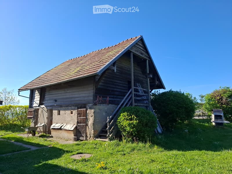 A rustic wooden and stone building with a pitched roof, wooden staircase, and a small garden area.