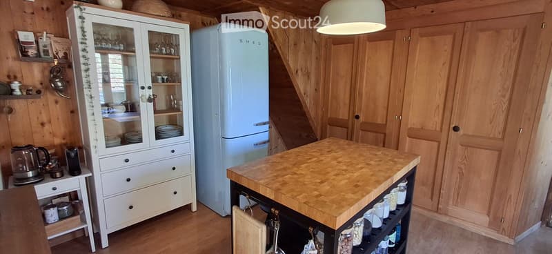 Cozy kitchen with wooden walls and flooring, featuring a white refrigerator, a wooden kitchen island, a white cabinet with glass doors, and various kitchen appliances and utensils.