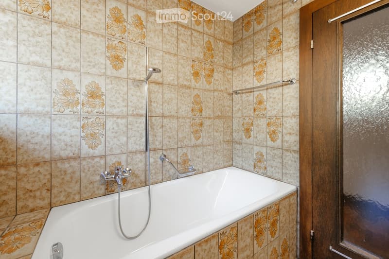 Bathroom with beige tiles featuring floral patterns, a white bathtub, a showerhead, and a glass shower enclosure.