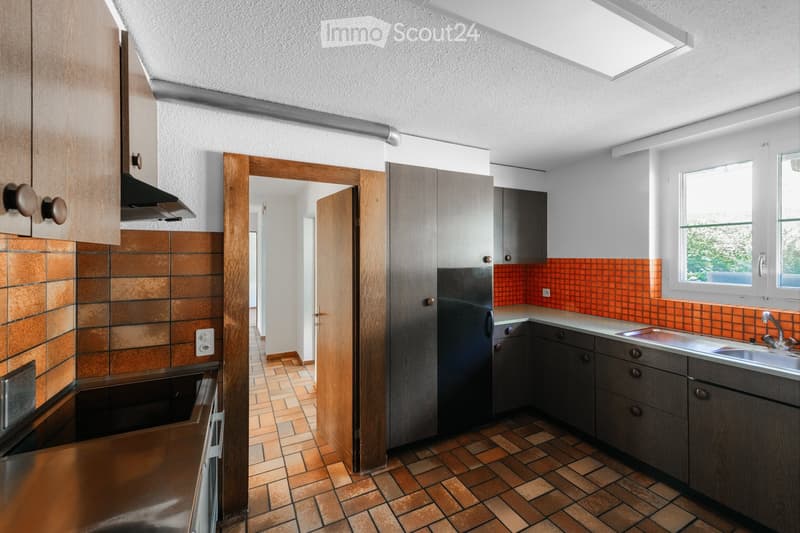 Modern kitchen with wooden cabinets, stainless steel appliances, and orange tiled backsplash. Features a sink, faucet, refrigerator, and oven.