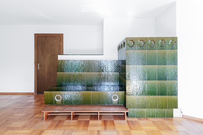 Minimalist room with green tiled fireplace, wooden bench, and a wooden door.