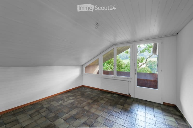 Empty room with white paneled ceiling, tiled floor, and large windows offering a view of greenery outside.