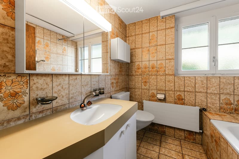 Bathroom with beige tiles, a large mirror, a sink with a modern faucet, a toilet, a bathtub, and a radiator.