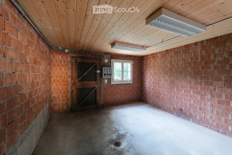 Empty room with exposed brick walls, wooden ceiling, concrete floor, and a single window. No furniture or equipment is present.
