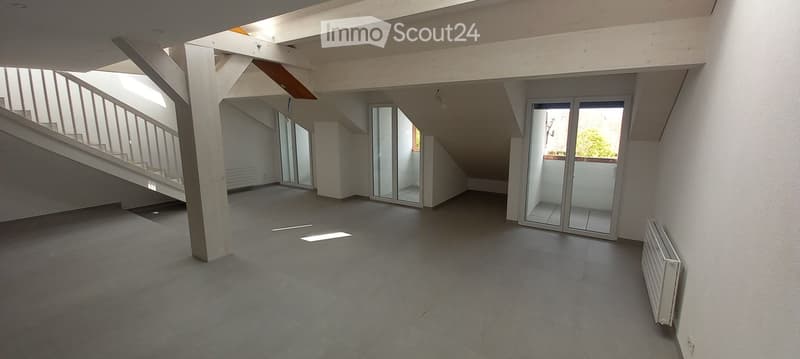Open, modern loft-style space with concrete floors, white walls, large glass doors leading to a balcony, and a staircase leading to an upper level.