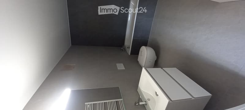 Modern bathroom with grey tiled walls and floor, white toilet, sink with mirror, and a radiator.